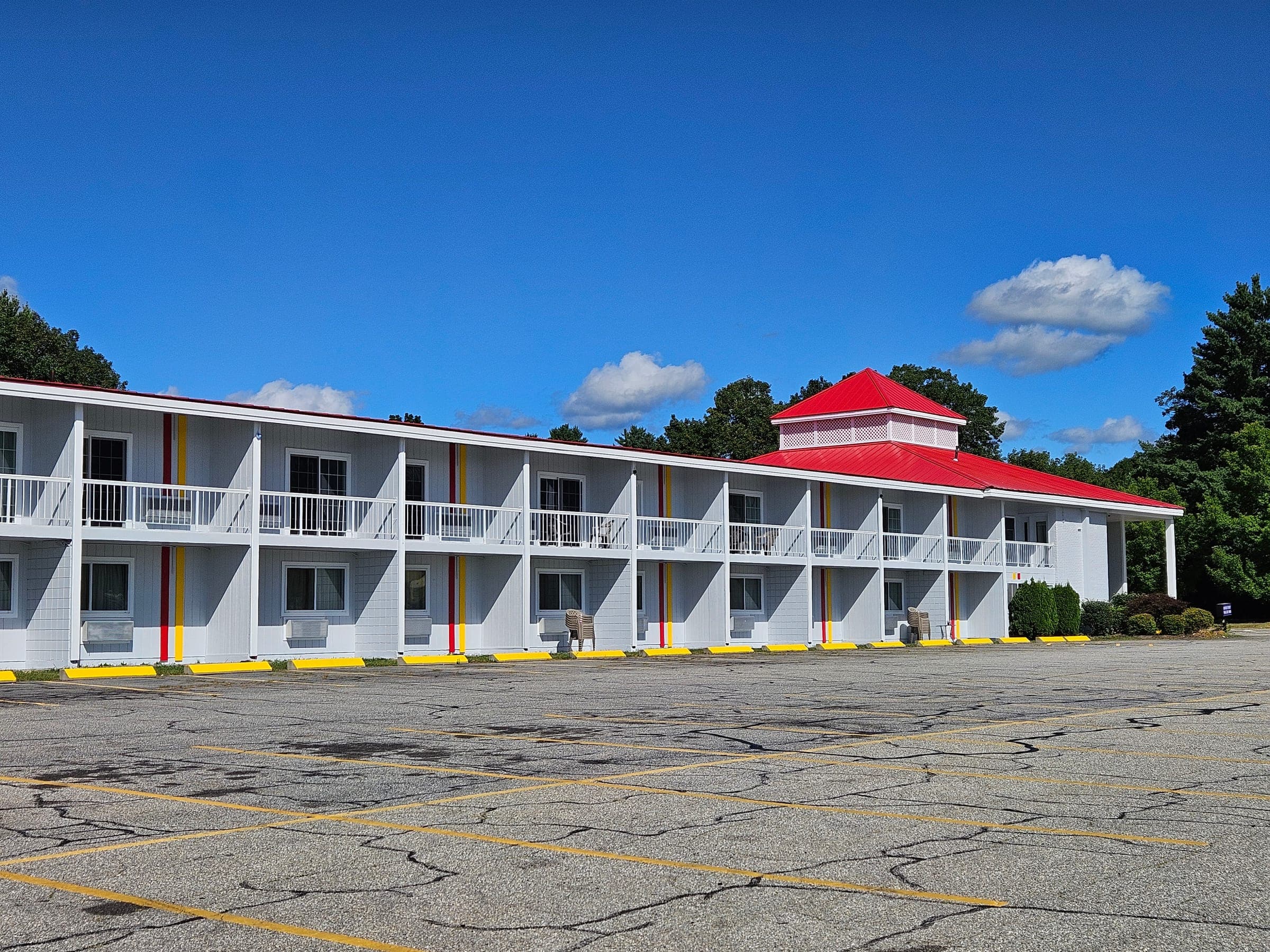 Saffron Inn front exterior on a summer afternoon — the white two-story motel with red trim, second-floor balconies, and red cupola roof at 170 Center Street, Auburn Maine