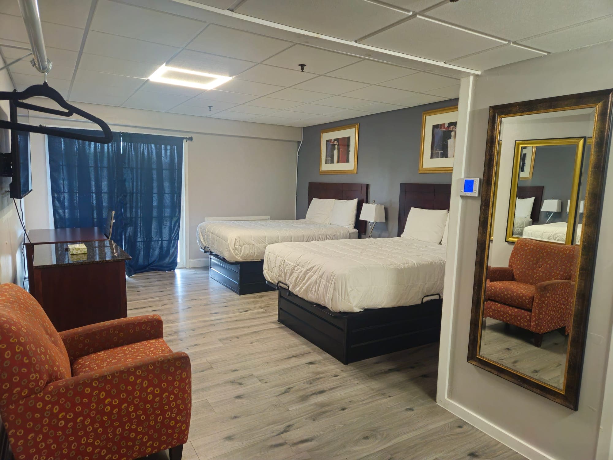 Saffron Inn two-double balcony room — two double beds with dark wood headboards, red armchair, sliding glass door with sheer blue curtains opening onto the balcony